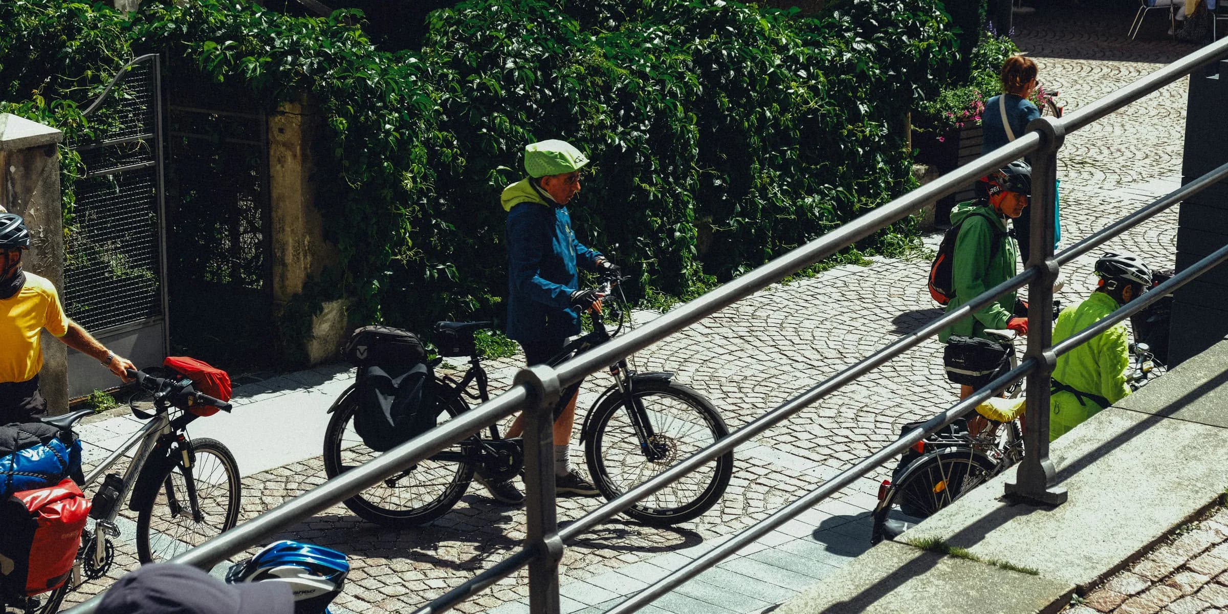 Cyclists with loaded bikes on cobblestone street.