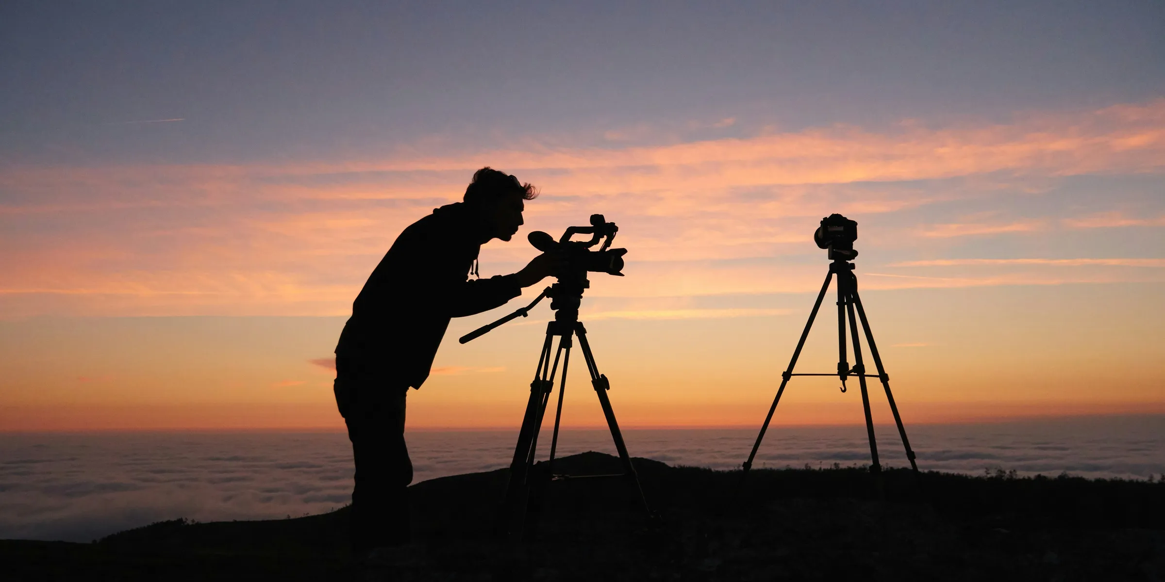silhouette photo of person holding camera on tripod stand outside