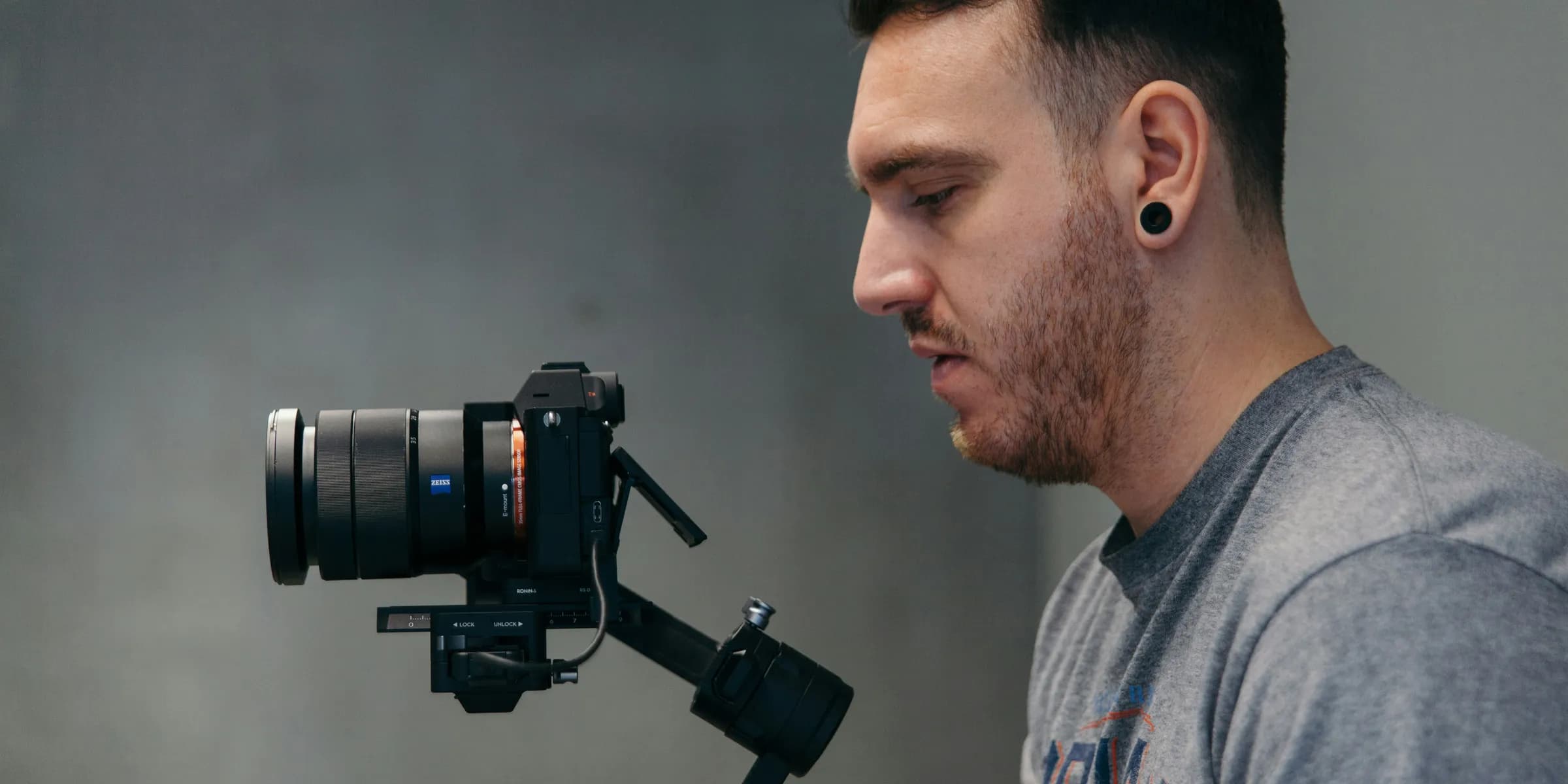 man wearing gray crew-neck shirt looking at black digital camera with camera stabilizer