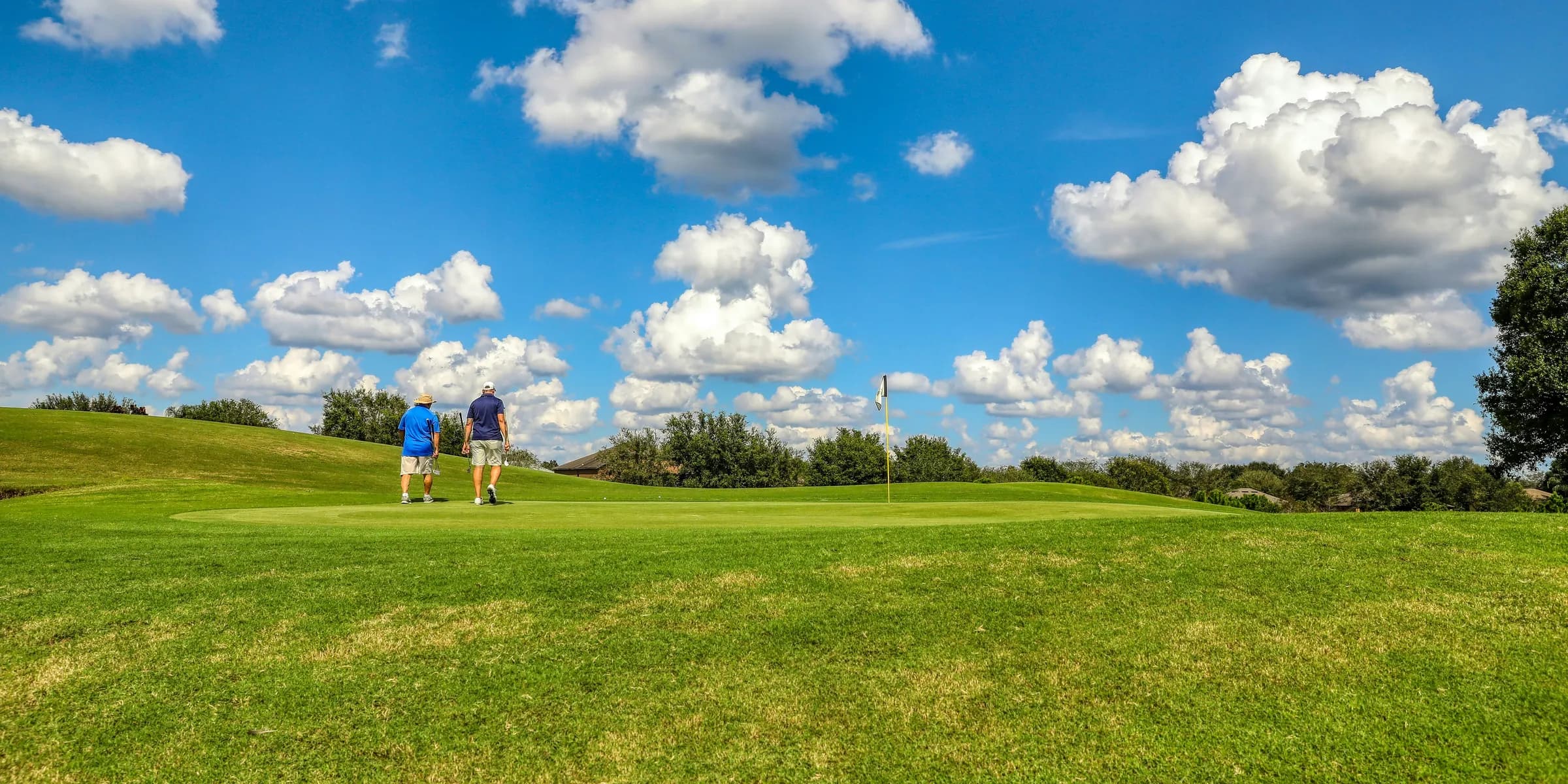 people playing golf on green grass field under blue and white cloudy sky during daytime