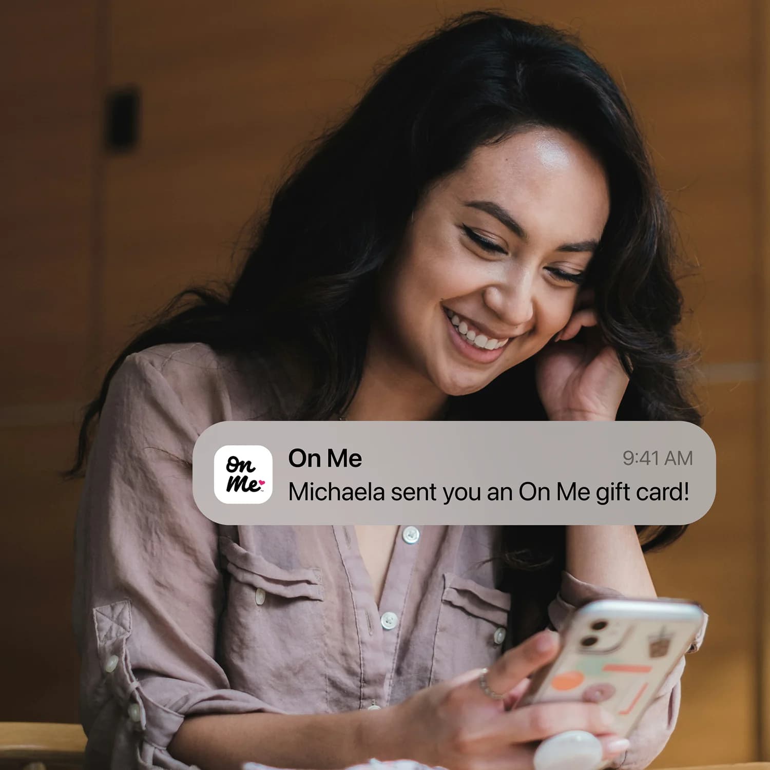 A picture of a woman smiling at a phone and receiving a scheduled On Me gift card