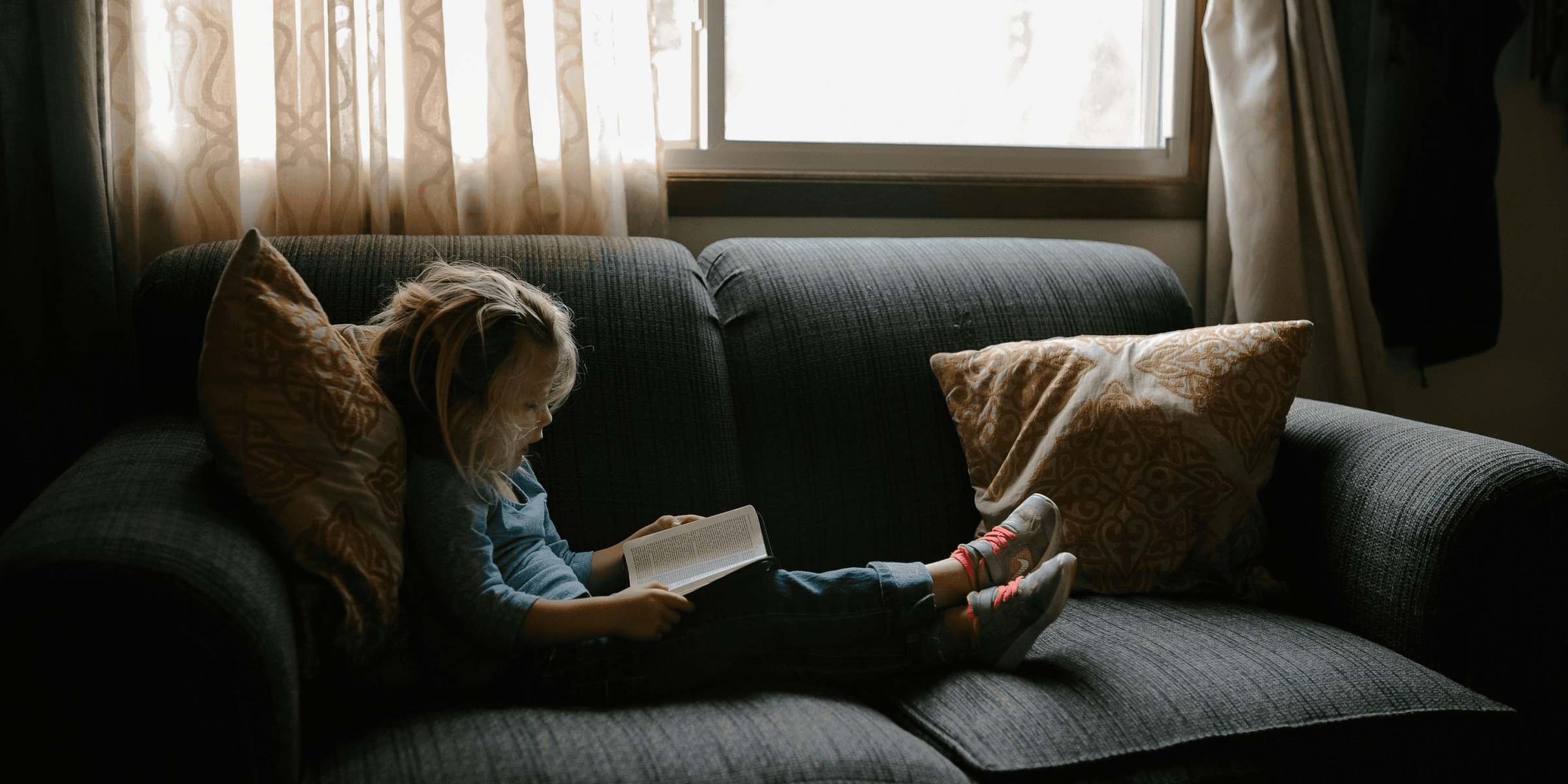 girl reading book sitting on sofa