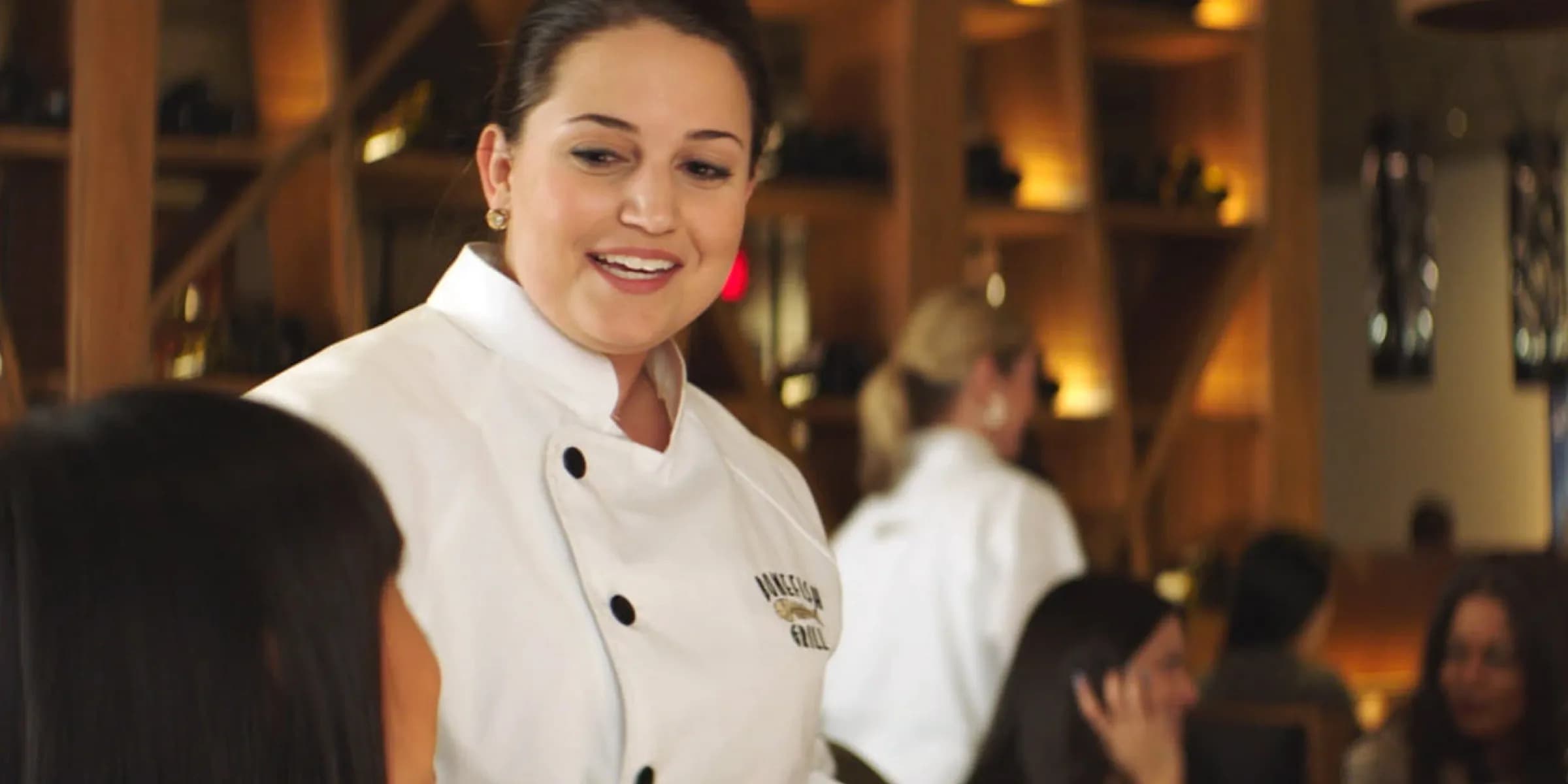 person in a chef's uniform smiling in a restaurant setting