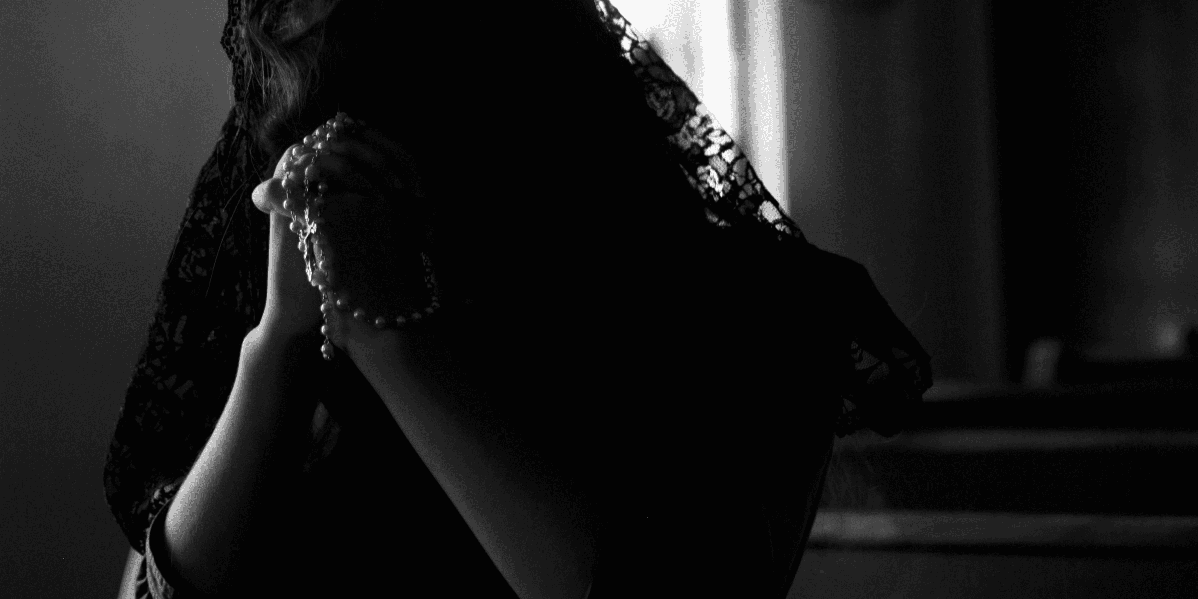 grayscale photography of woman praying while holding prayer beads