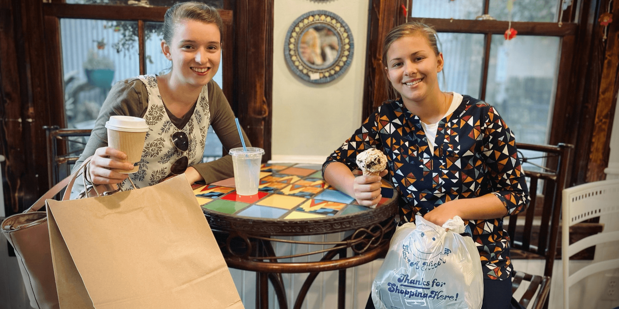 a couple of women sitting at a table with paper bags.