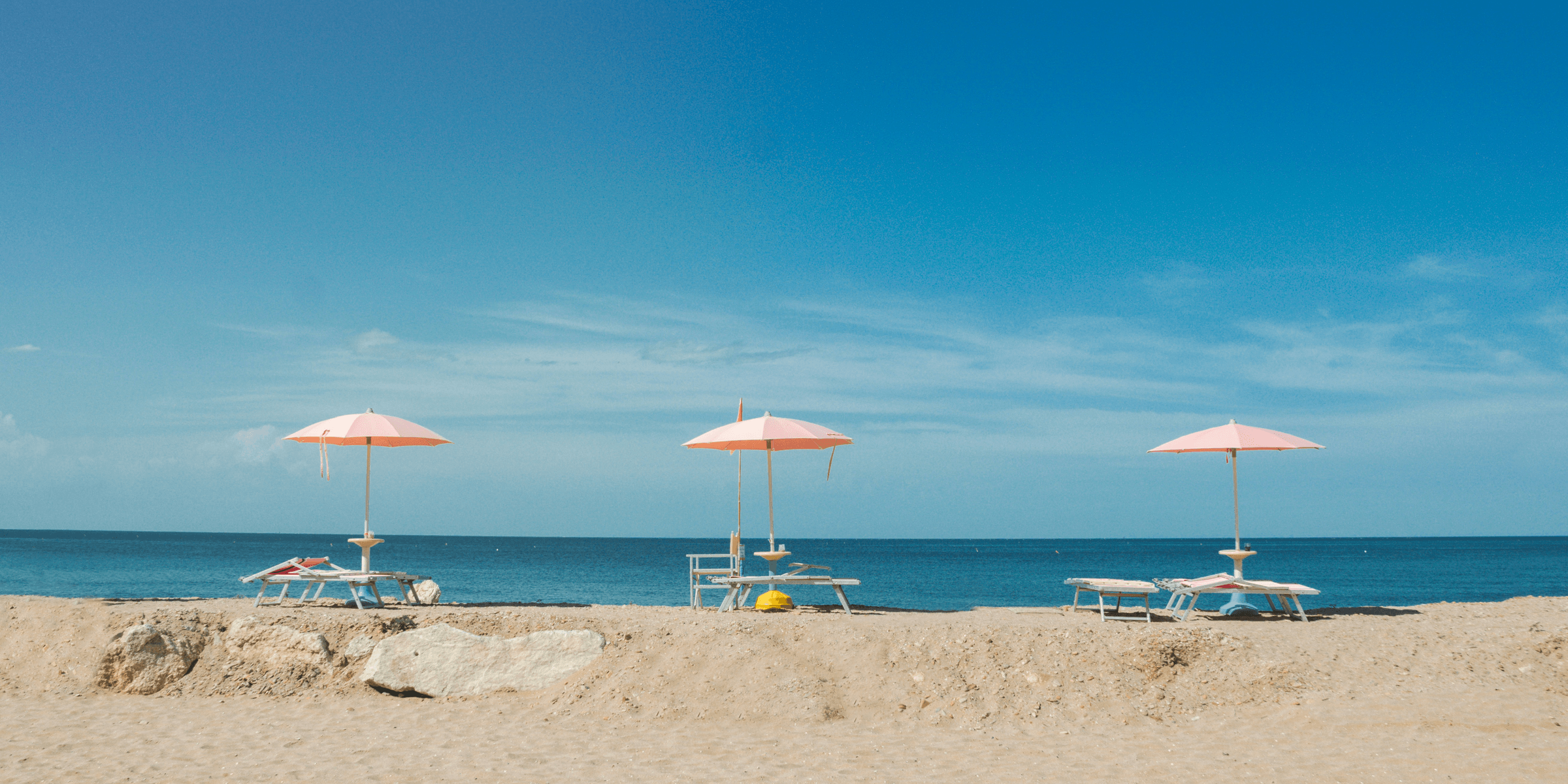 three empty beach loungers with umbrellas overlooking the beach under blue sky.