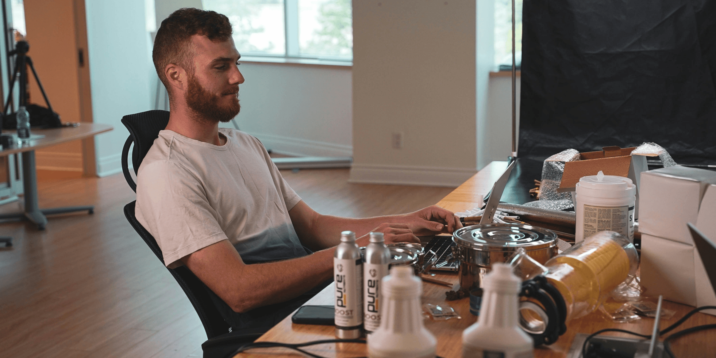 a man sitting at a desk with a computer and a group of bottles.