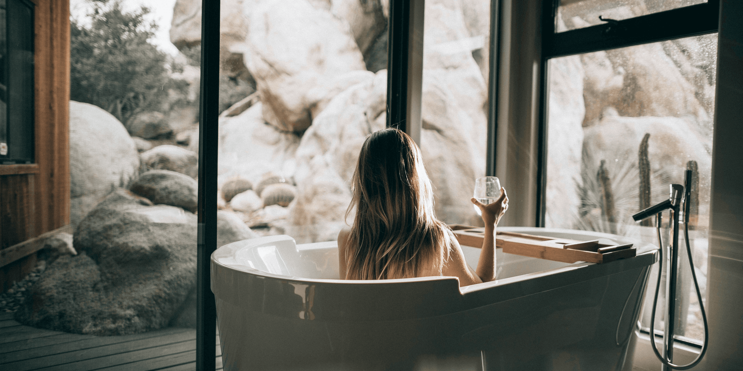 woman in white bathtub holding clear drinking glass.