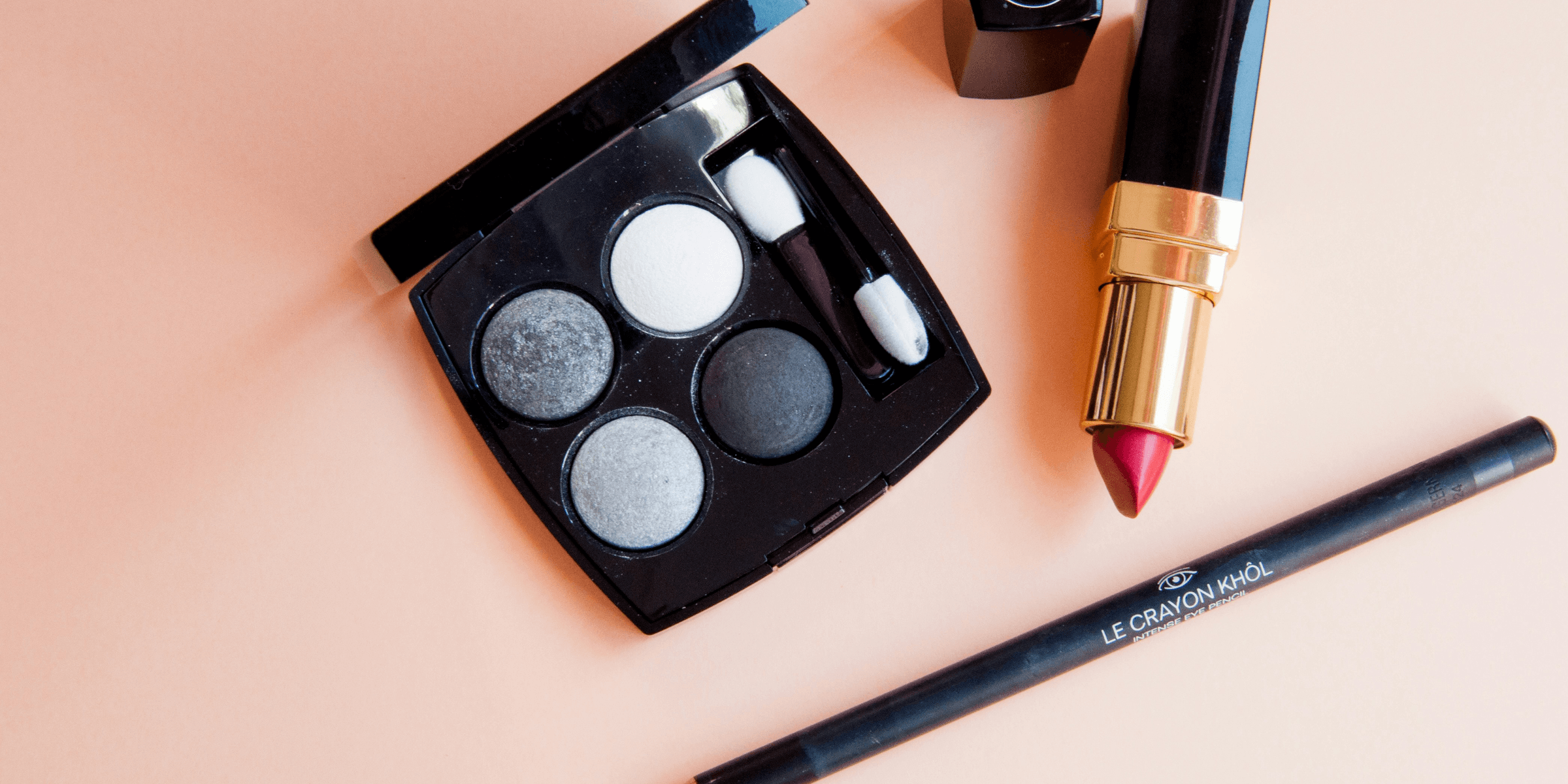 a lipstick, eyeliners, and lipstick brush on a pink surface.