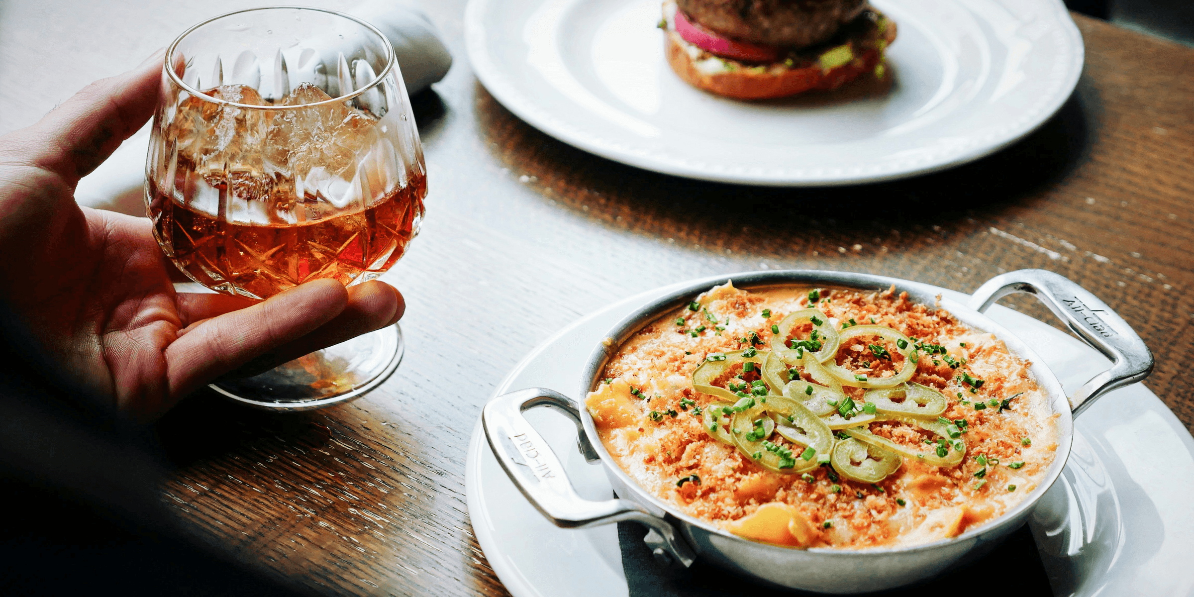 person holding clear snifter beside bowl of soup.