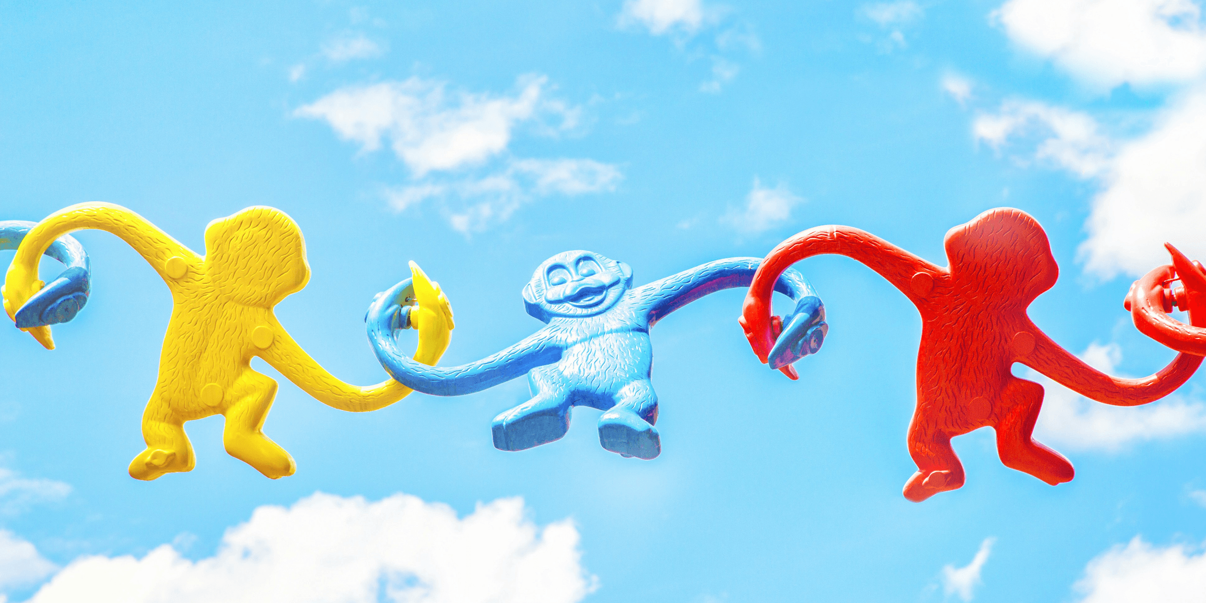 three assorted-color monkey plastic toys holding each other during daytime.