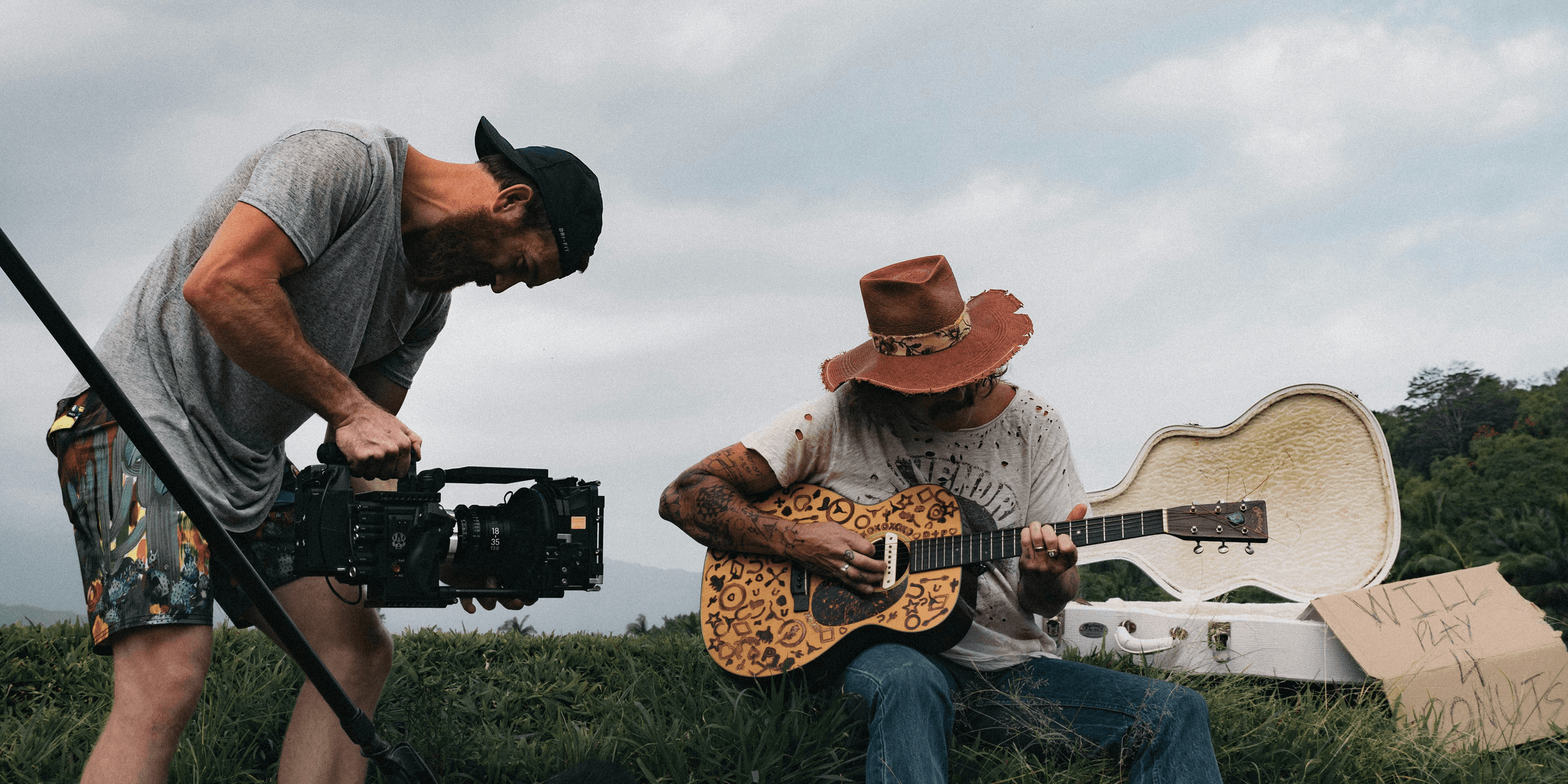 man playing guitar beside man holding video camera during daytime.