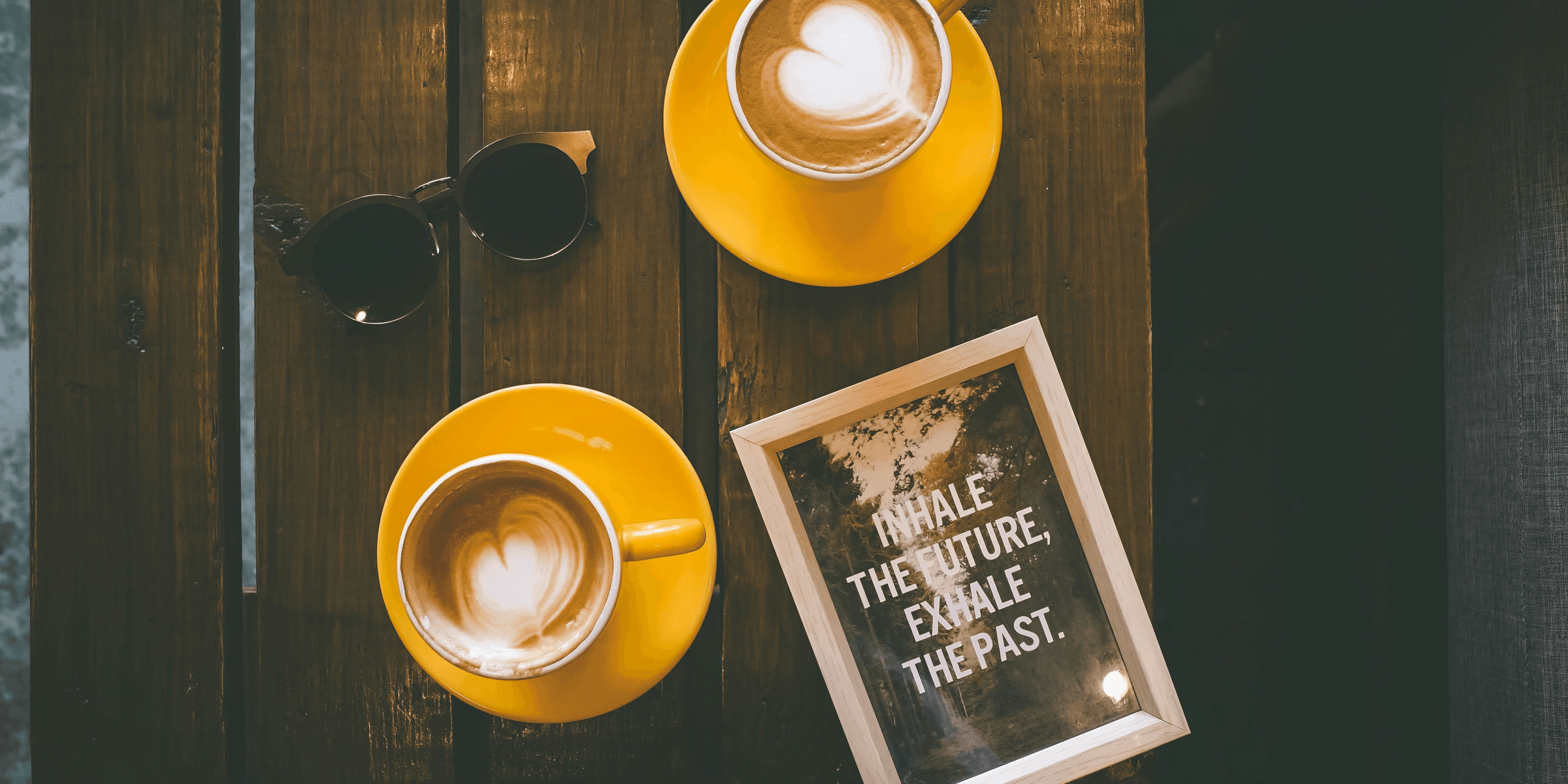 two coffee lattes in yellow cup with saucer on brown wooden table.
