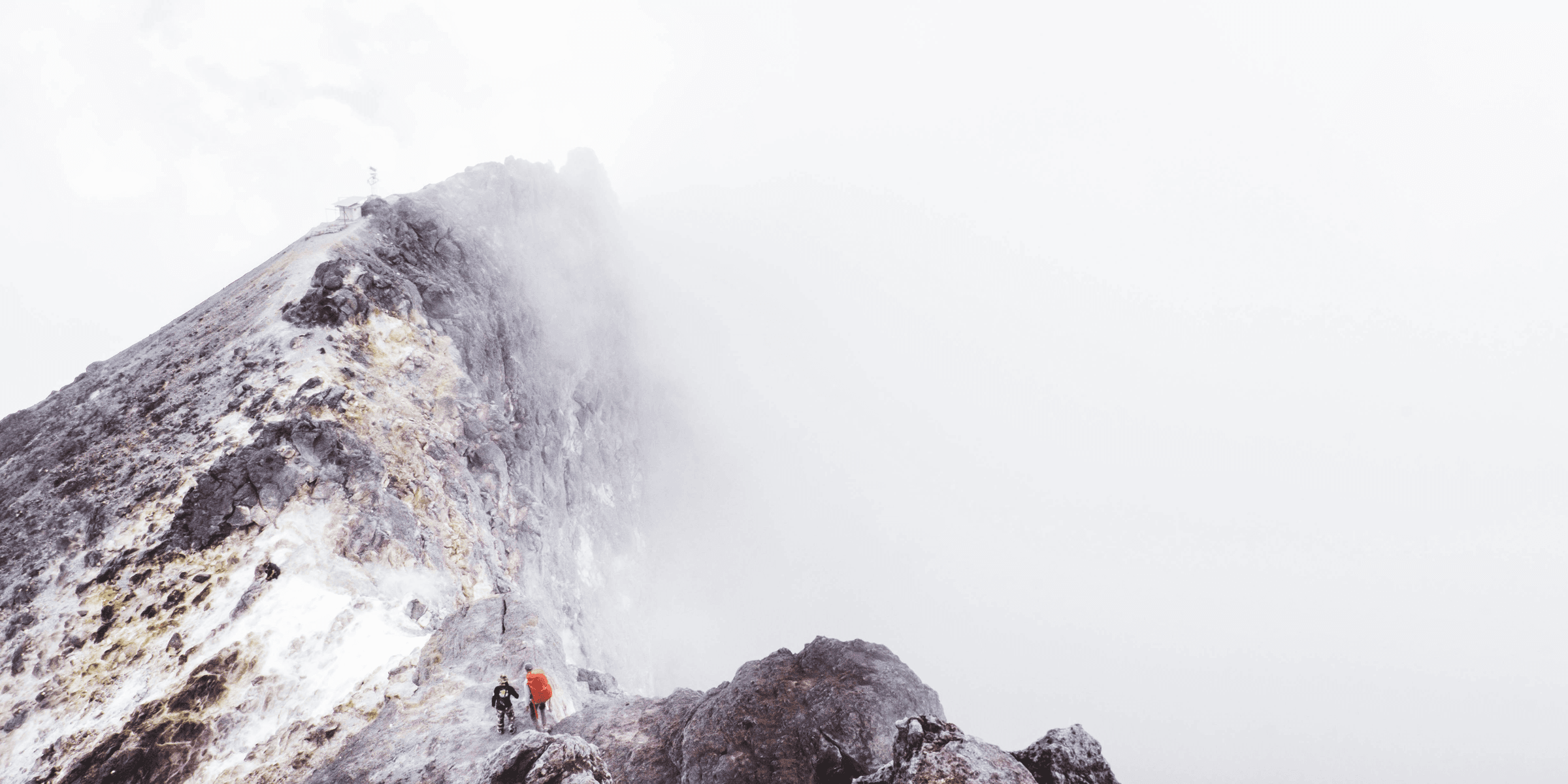 two people standing on mountain slightly covered with fogs during daytime.