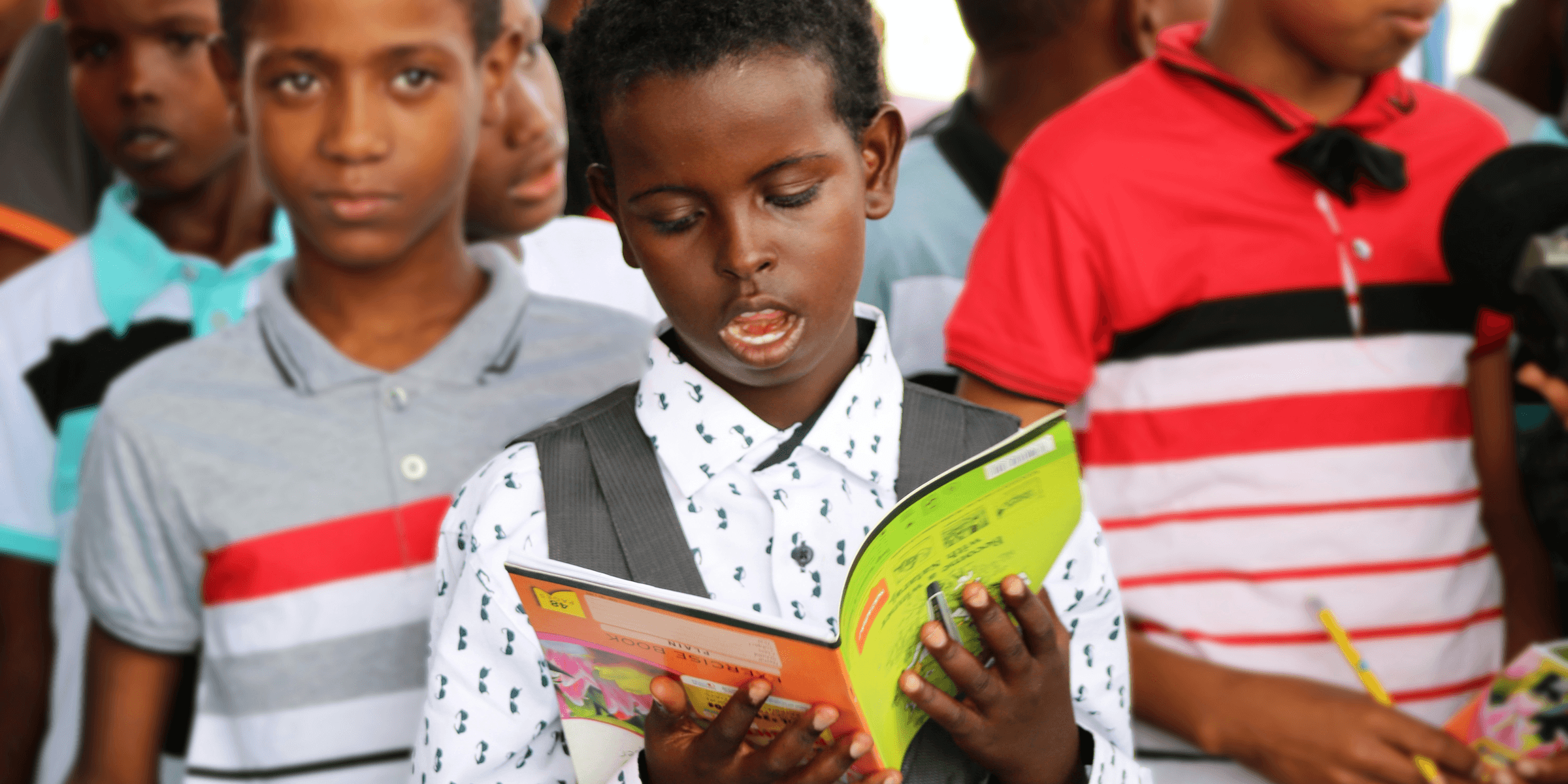 man in red and white polo shirt holding yellow book.