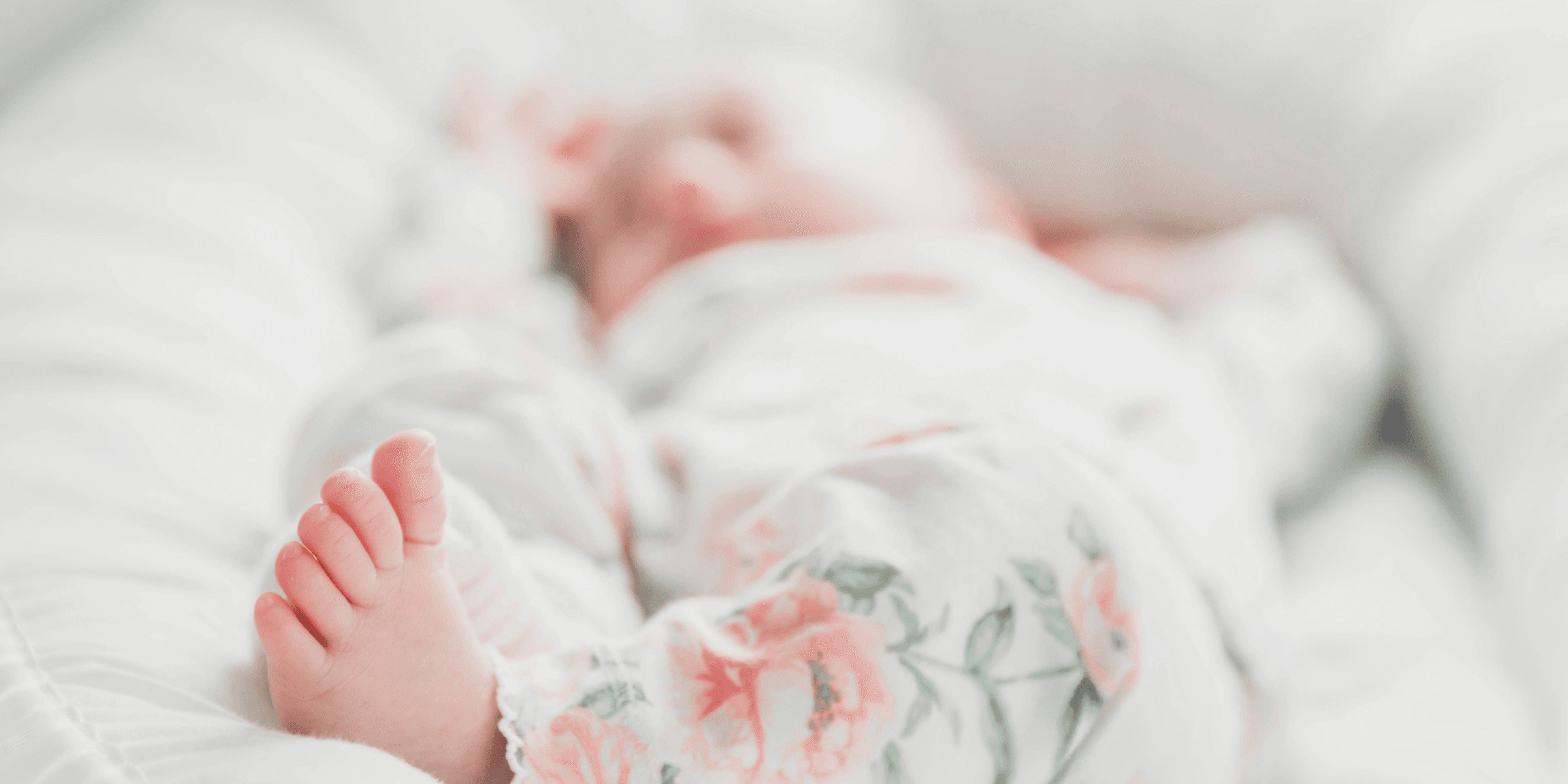 baby in white and red floral onesie lying on bed.