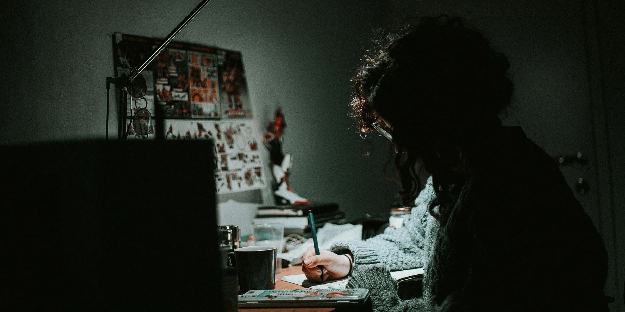 low light photography of woman in gray knit sweatshirt writing on desk