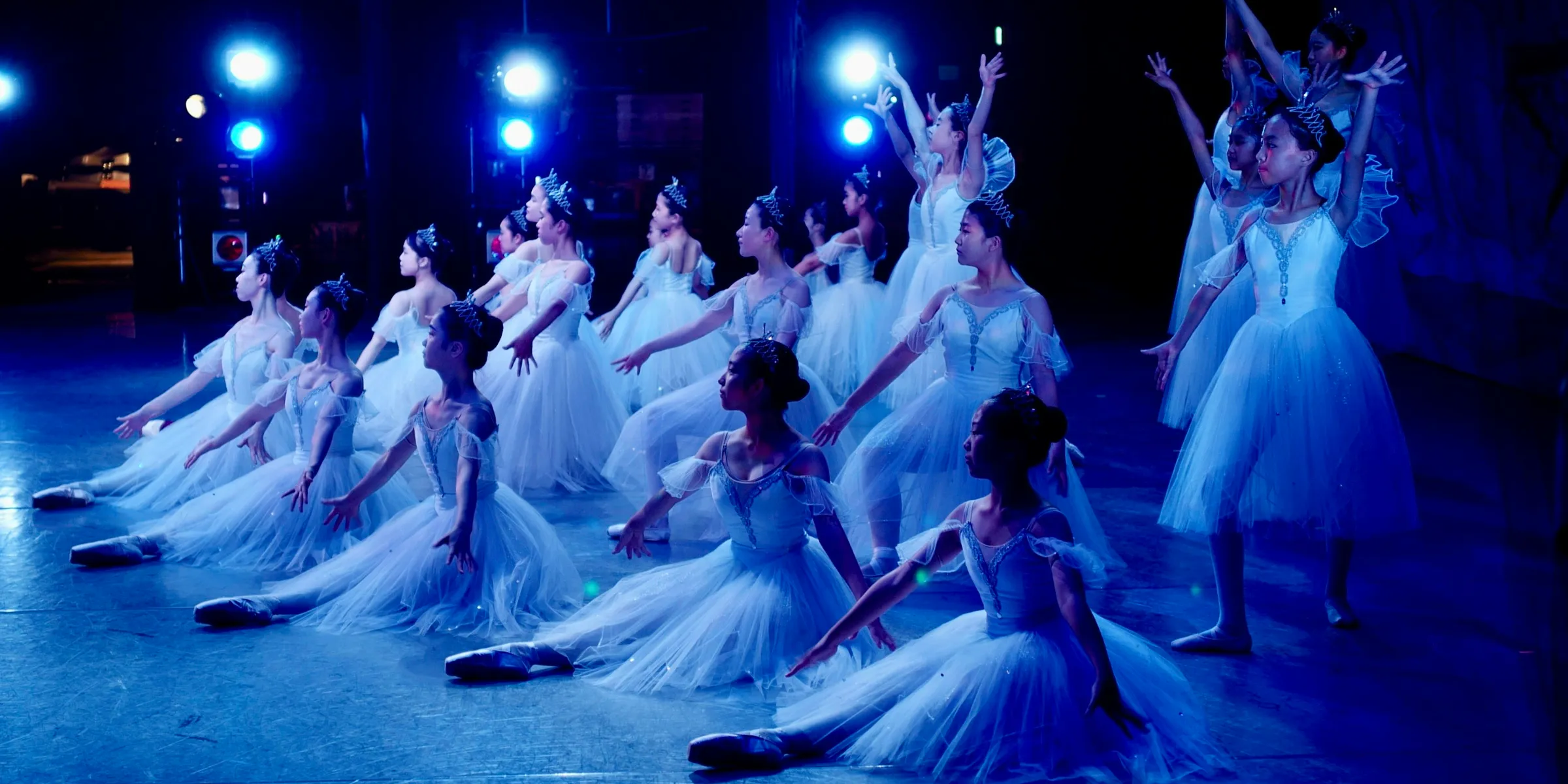 Ballet dancers in white tutus perform on stage.