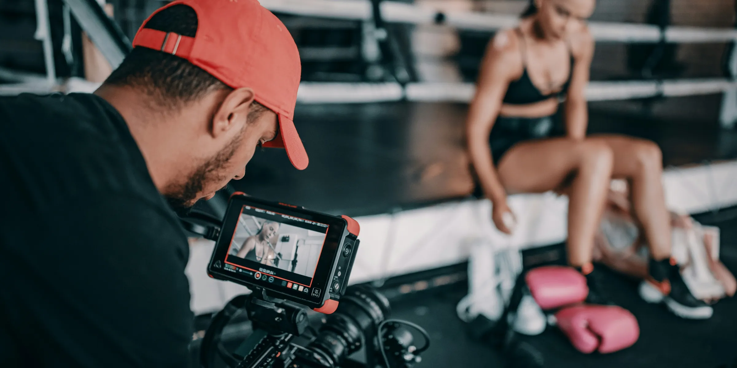 man taking video of woman wearing black bra and black shorts while sitting near pink boxing gloves