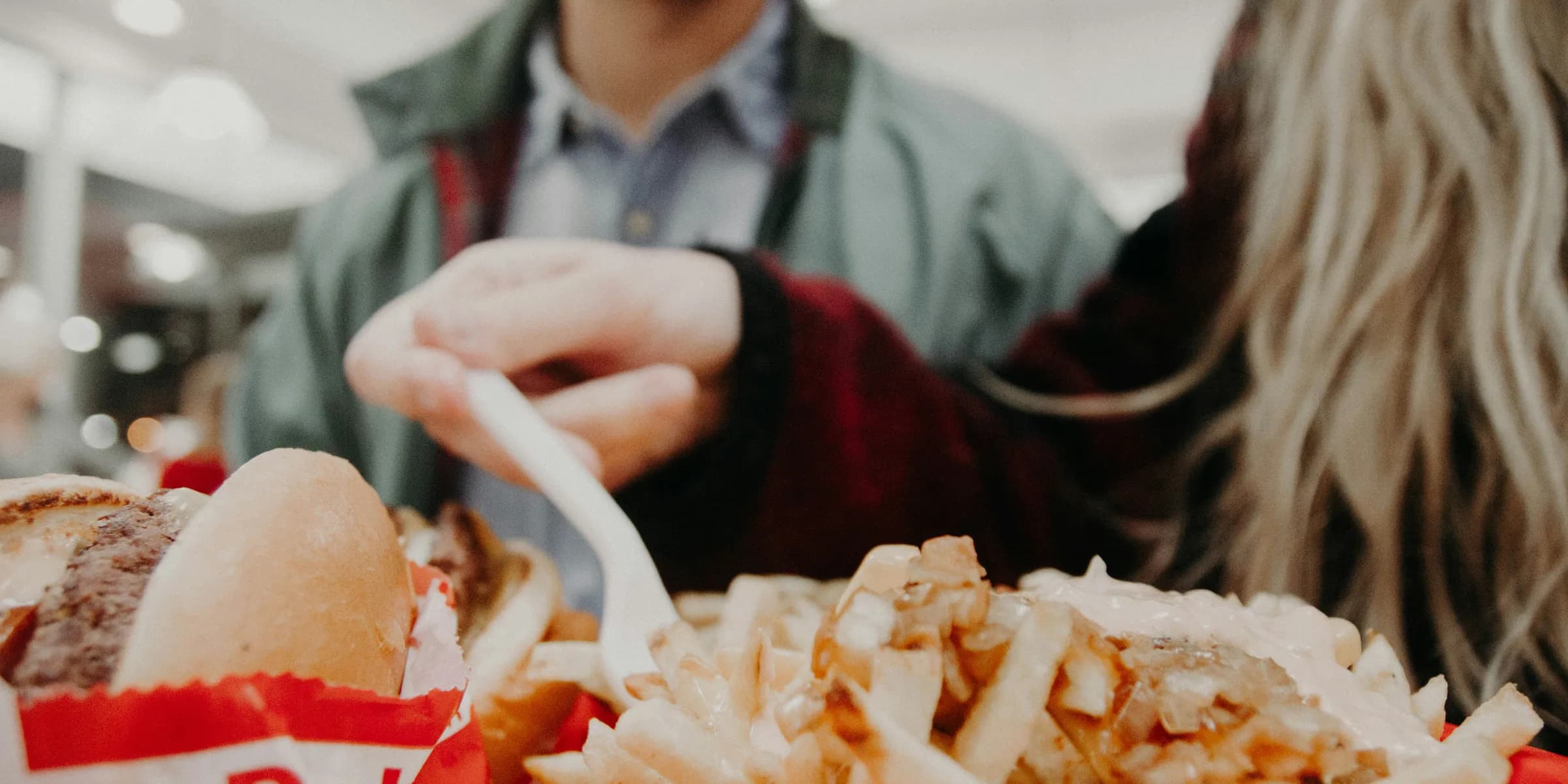 woman in maroon long-sleeved shirt holding fork over fries