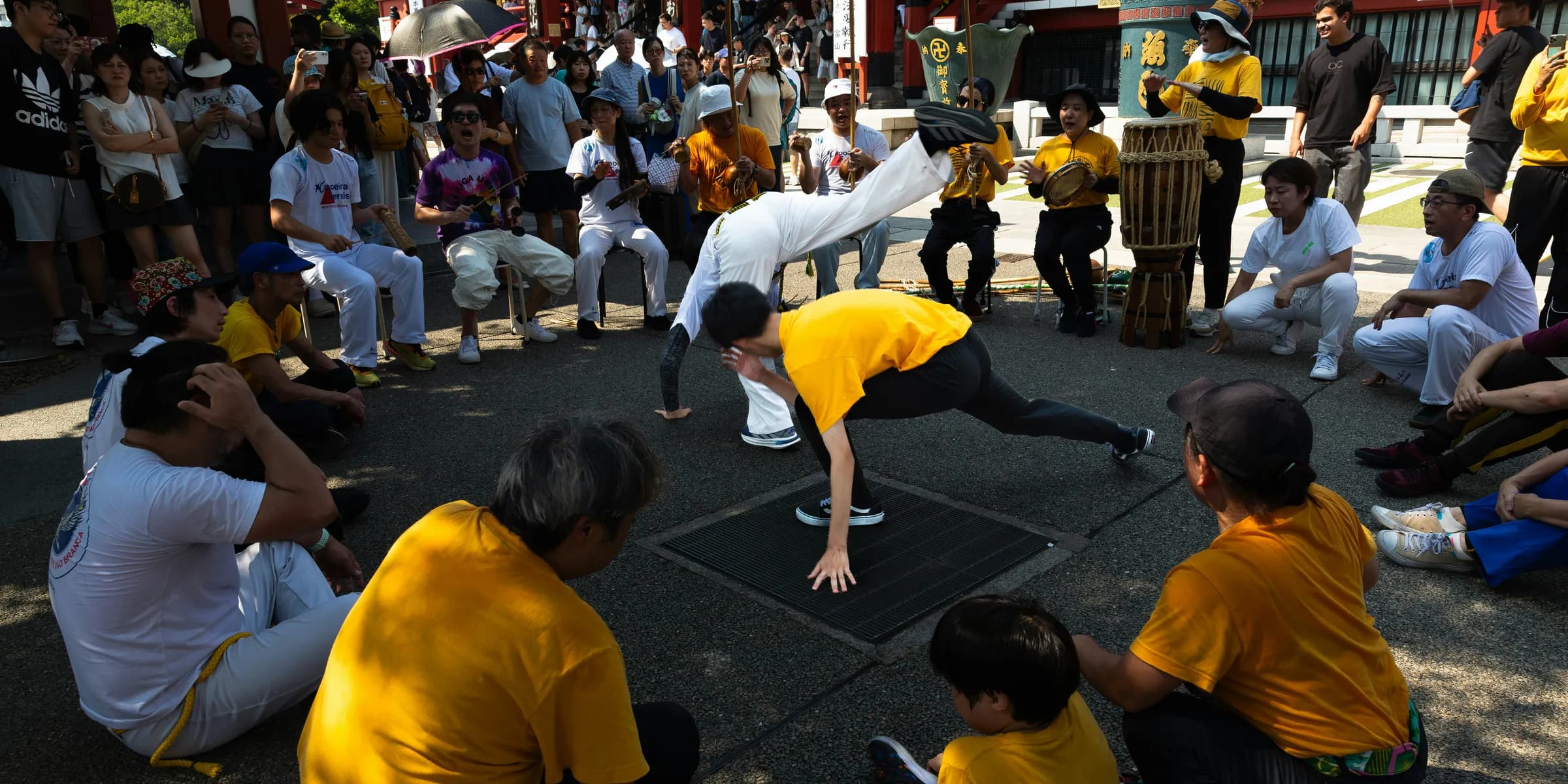 People watch capoeira performers in a circle outdoors.