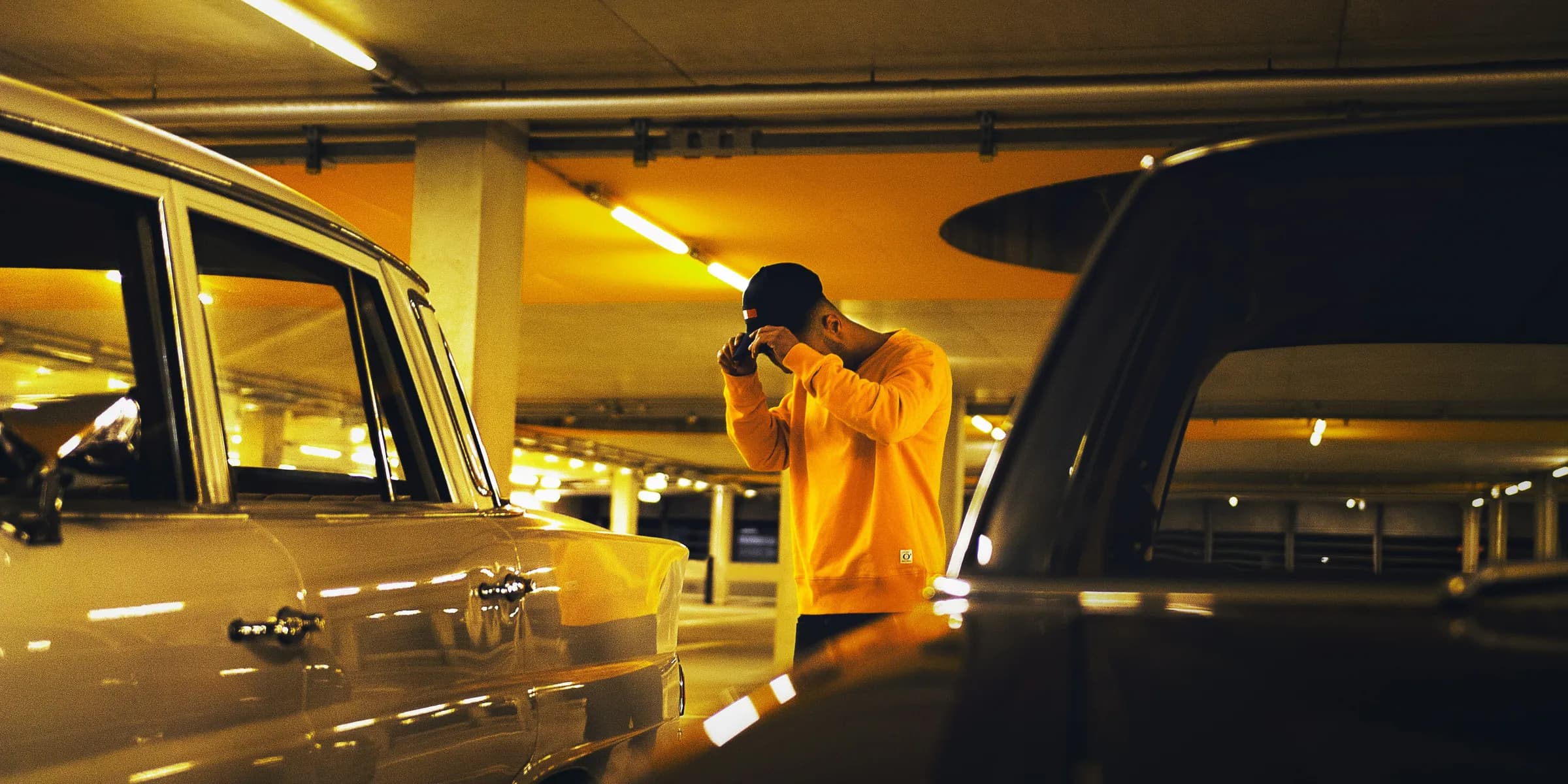 man holding cap standing between car on parking lot
