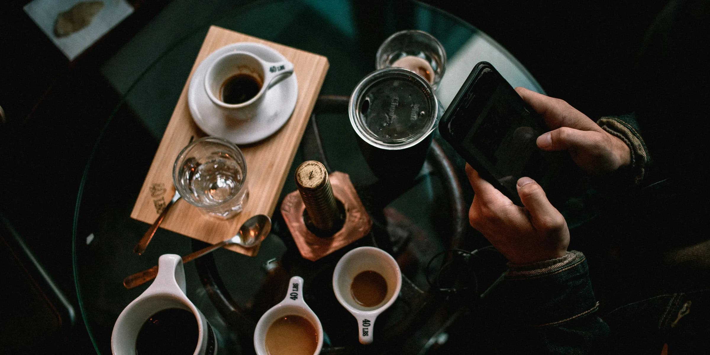 person holding black smartphone near white ceramic mug on table
