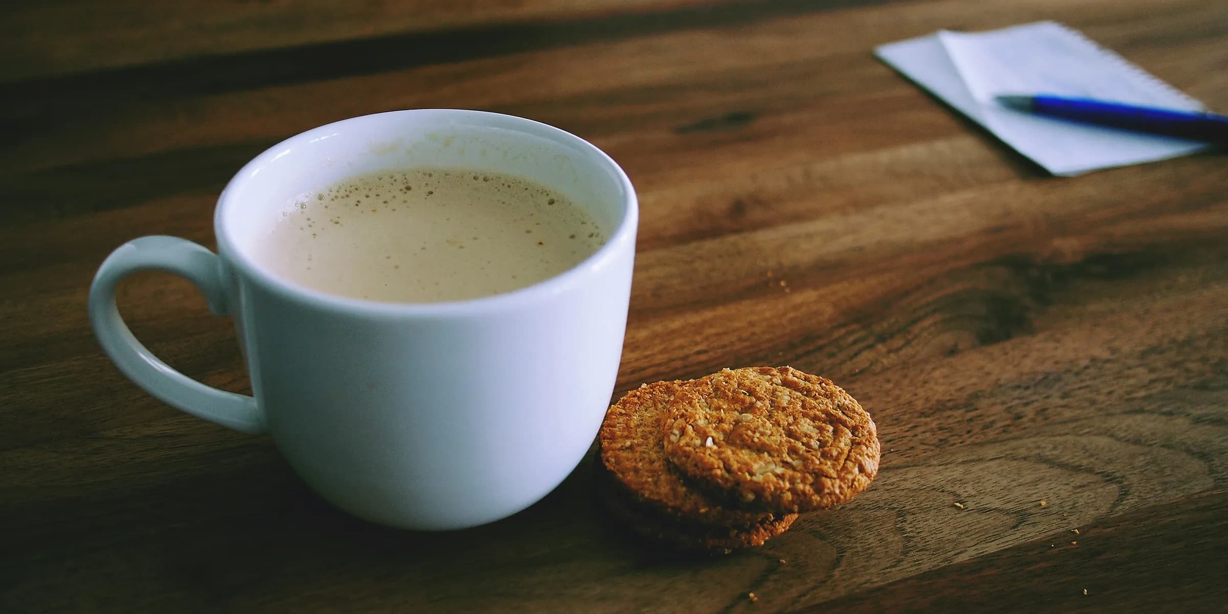 shallow focus photography of white ceramic mug beside two baked cookies on brown wooden board