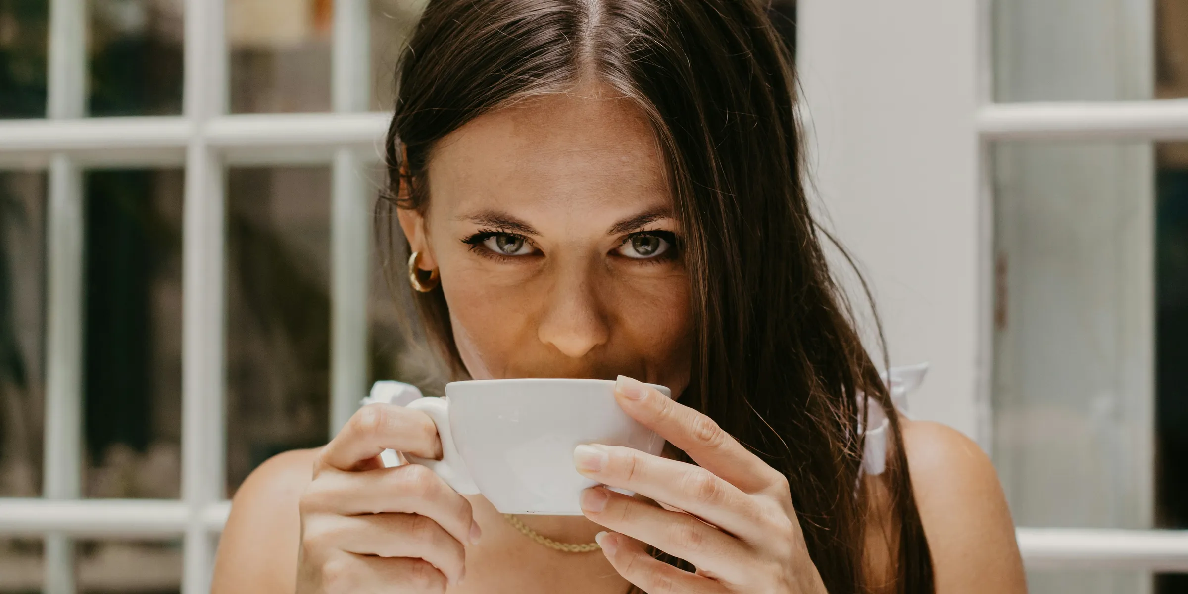 a woman drinking from a cup in front of a window