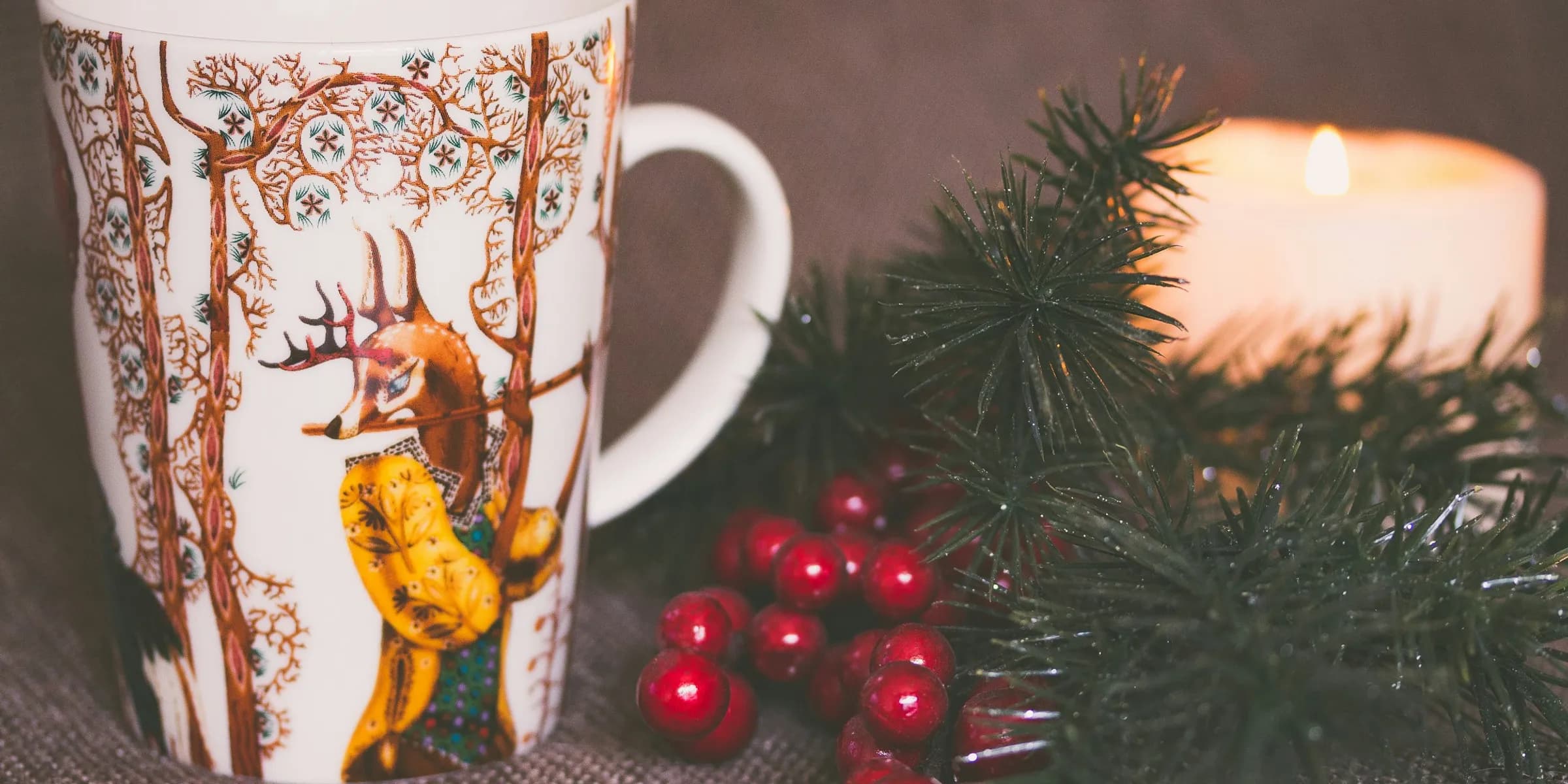 white and brown print ceramic mug near red mistletoe and candle