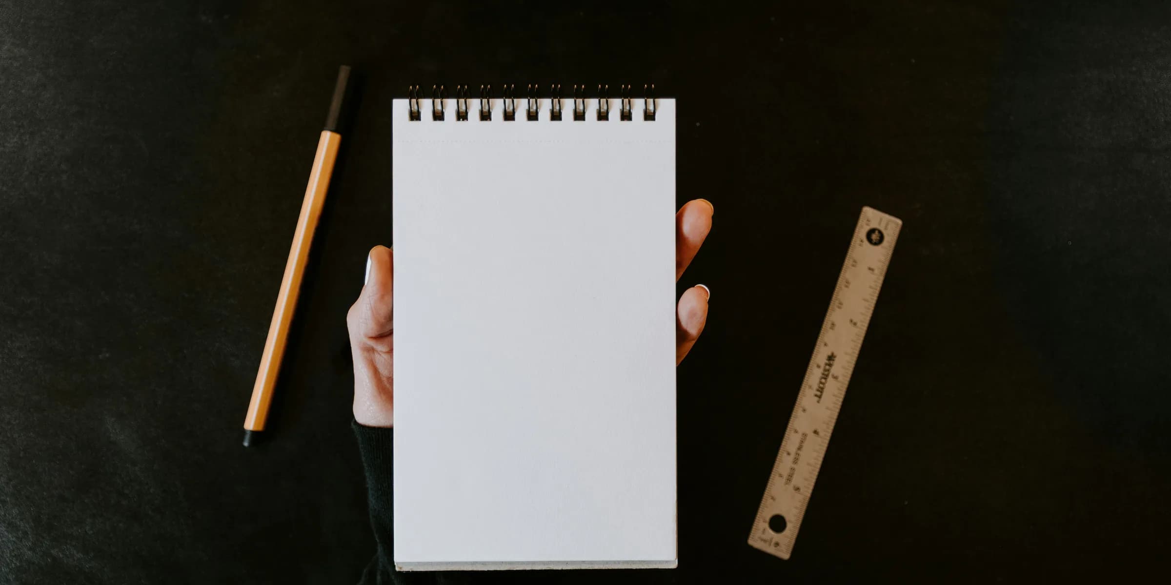 a person holding a notebook with a pencil next to it