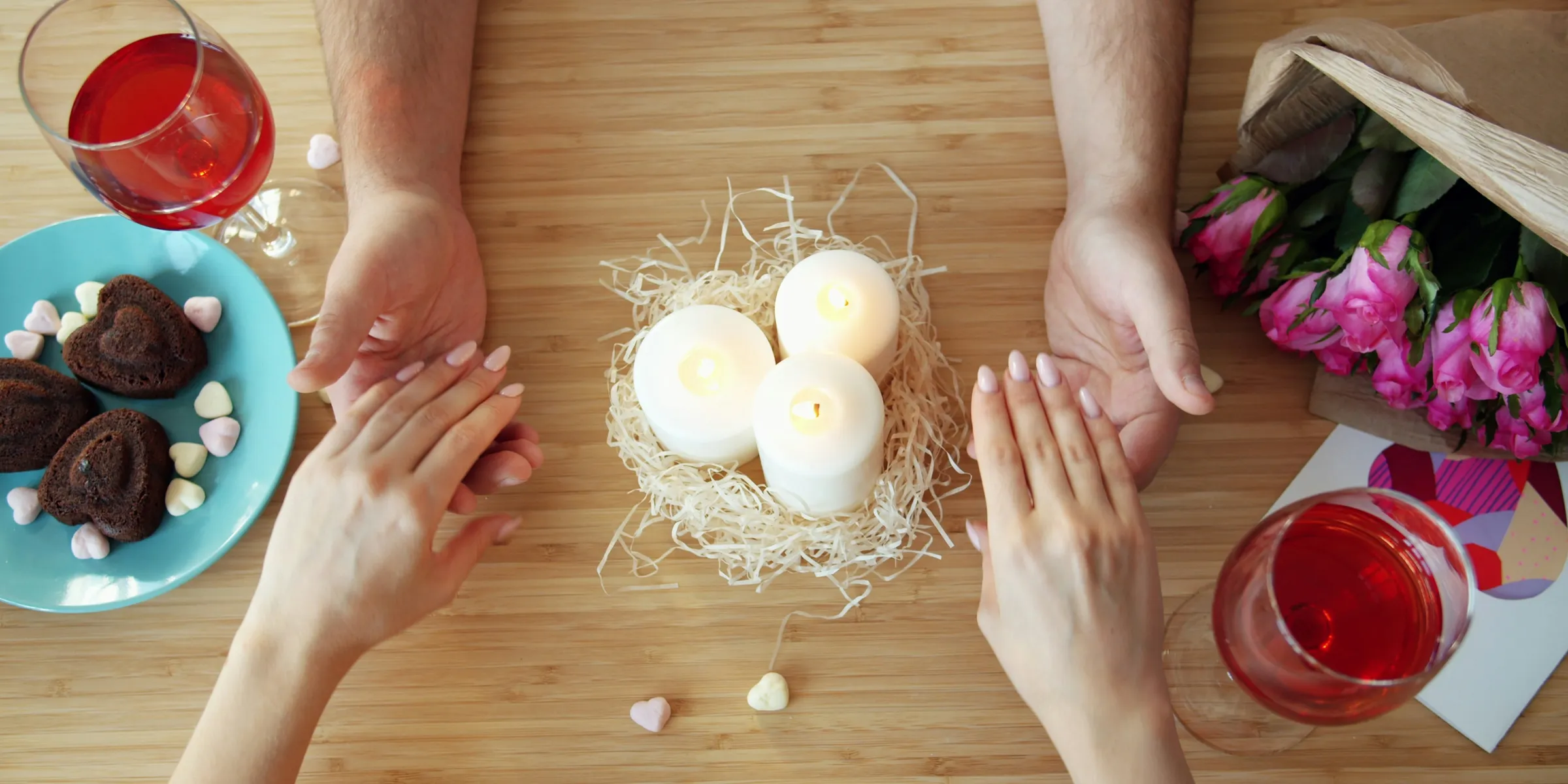 Couple holding hands over romantic dinner table with candles.