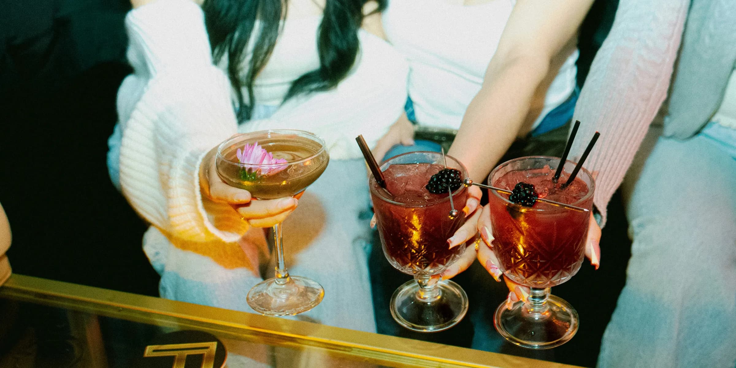 Friends hold cocktails, enjoying a night out.