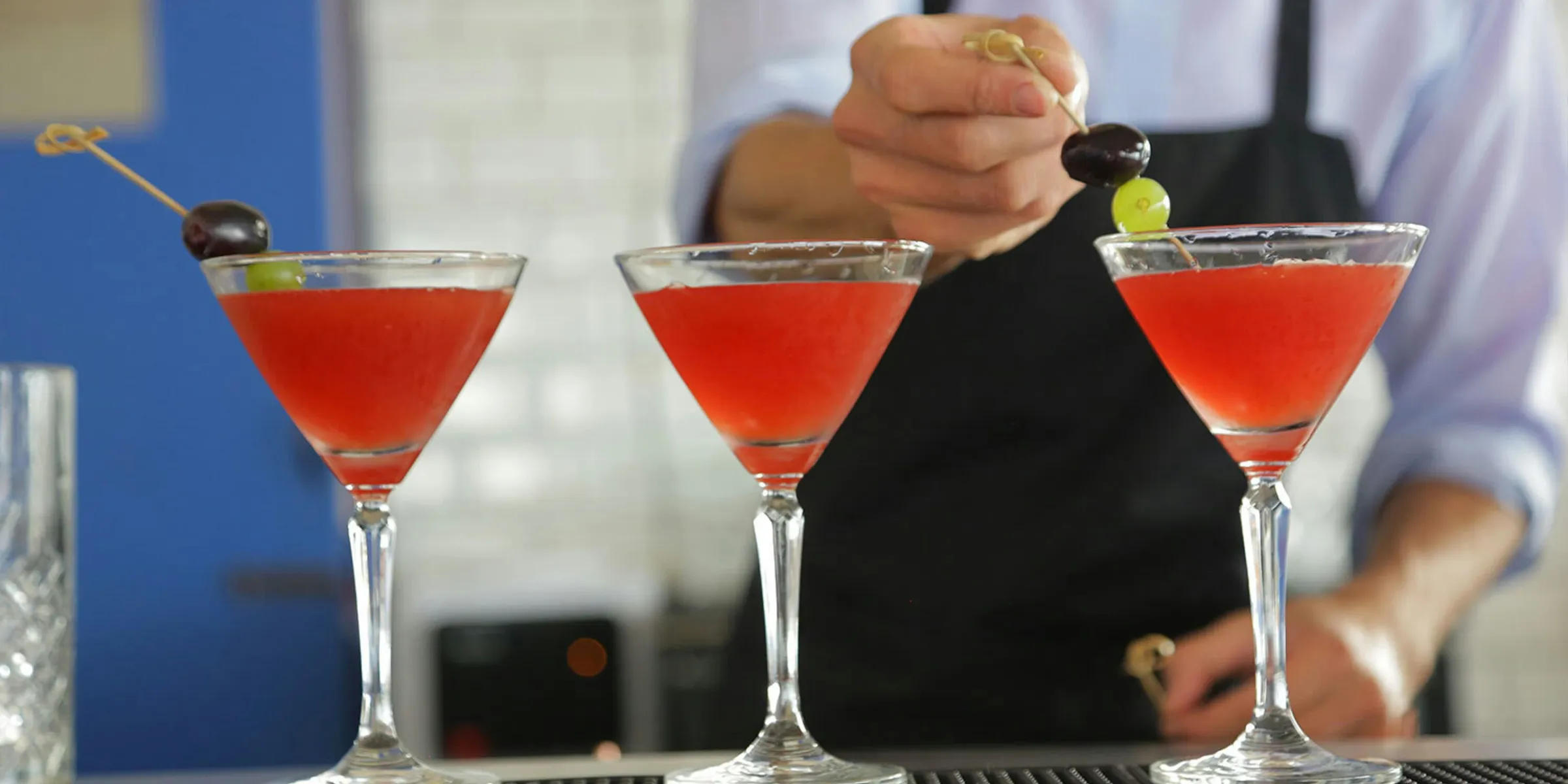 Bartender garnishing three red cocktails with grapes.