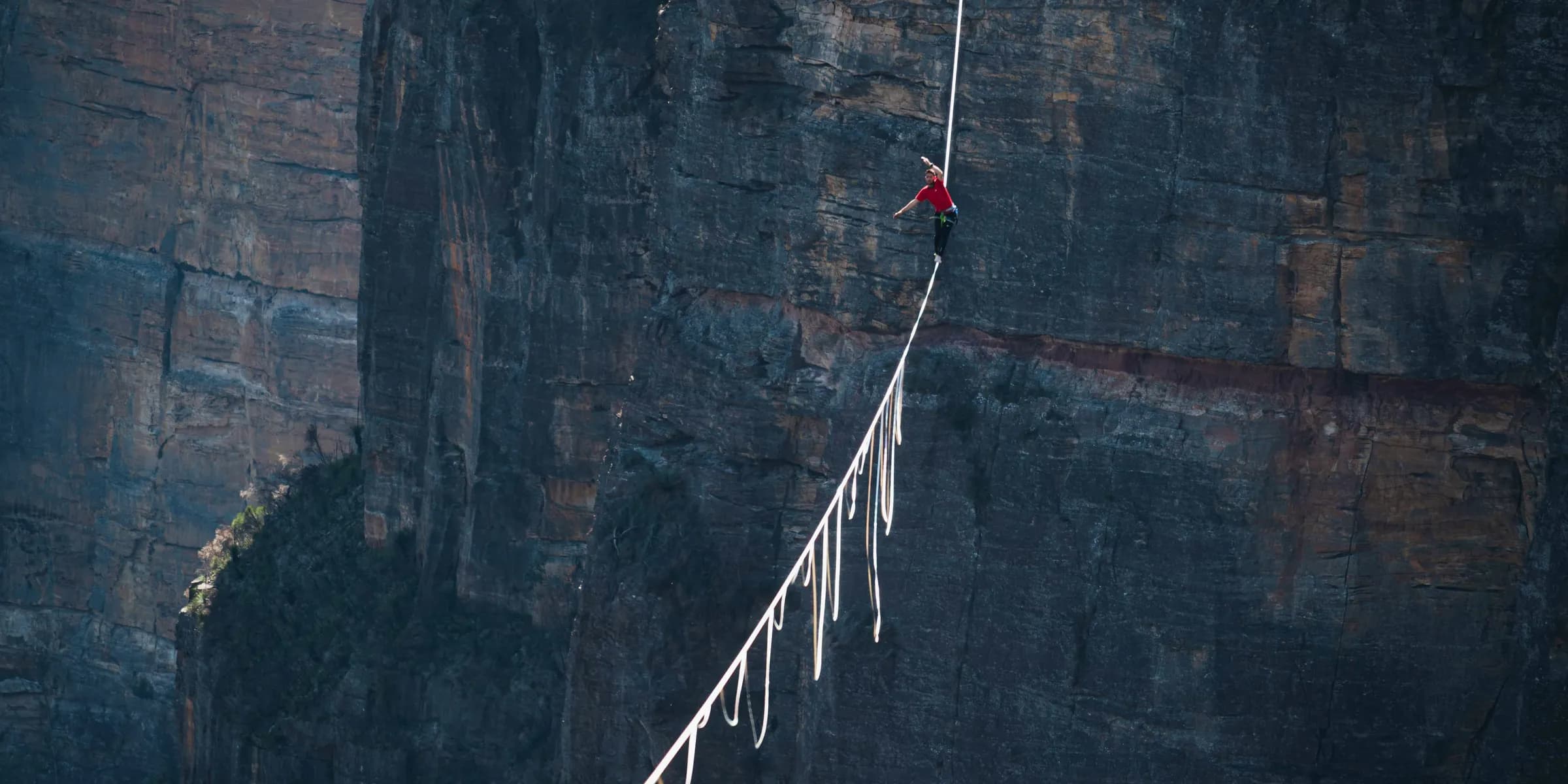 a man walking across a rope on top of a cliff