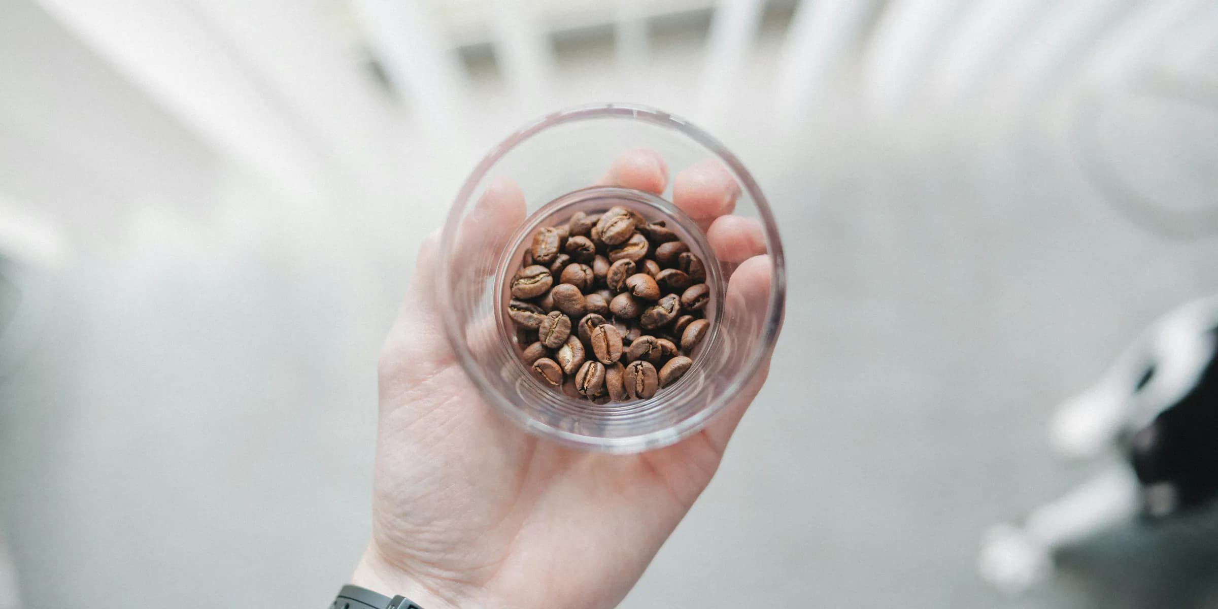 person holding clear drinking glass with filled of coffee beans