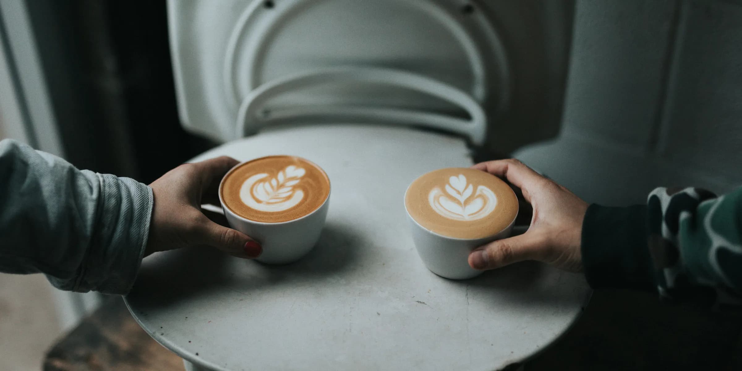 two person holding cappuccino coffee cups