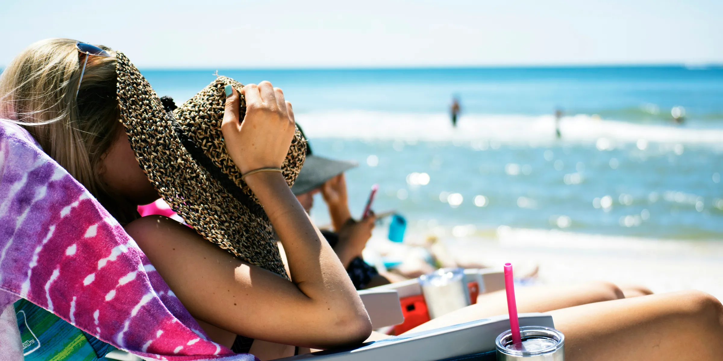 woman lying on sun lounger covering her face with straw hat near sea
