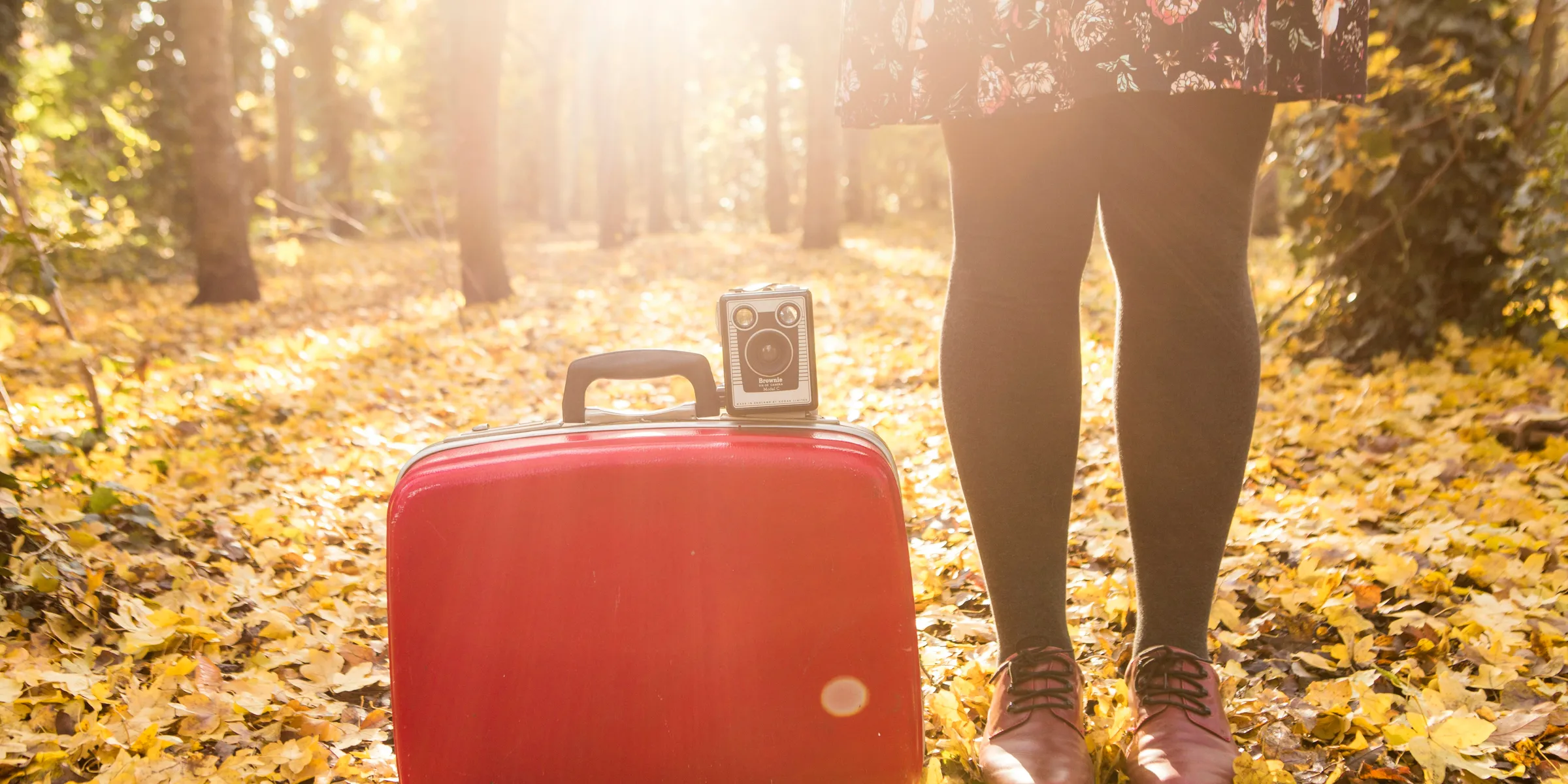 woman standing beside red suitcase and camera