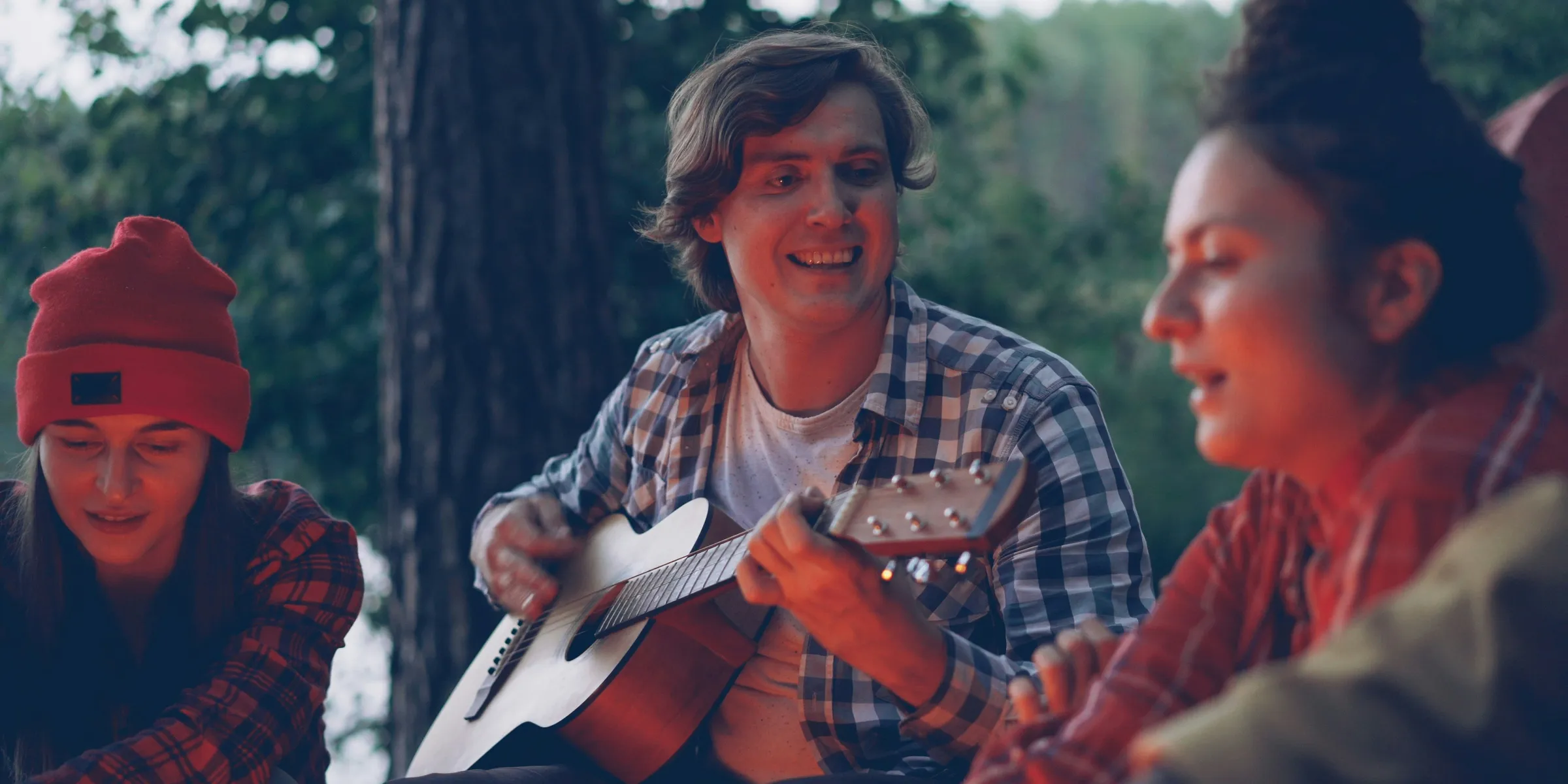 Friends gathered around campfire playing guitar and singing